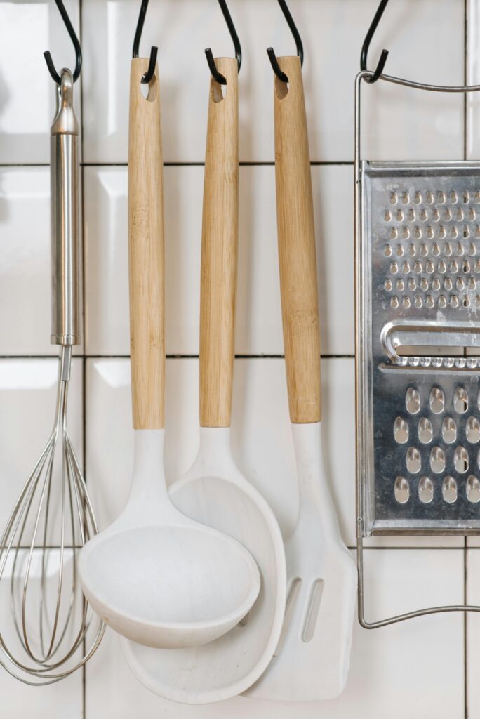 pexels-photo-6996092-6996092 Aesthetic arrangement of kitchen utensils including a whisk, ladle, spatula, and grater on a tiled wall.